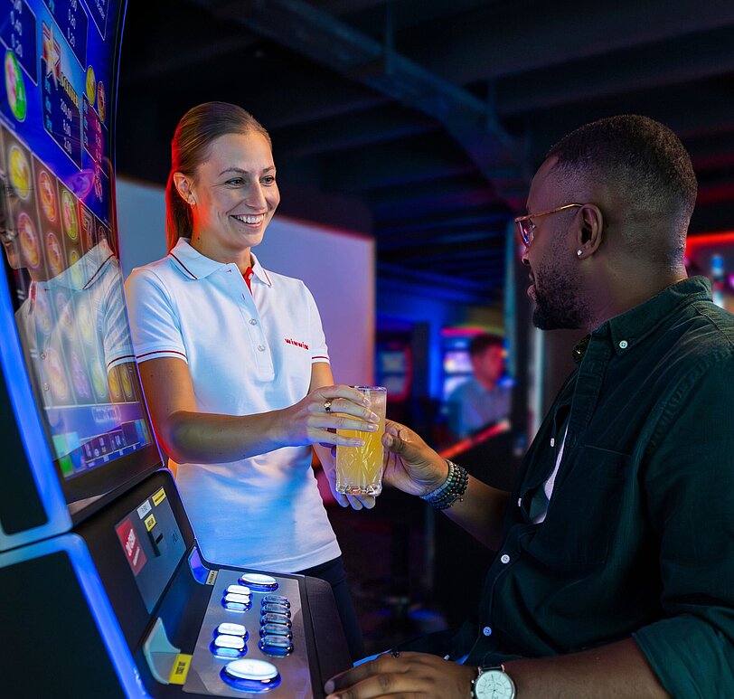 WINWIN Mitarbeiterin serviert einem Gast ein Getränk am Spielautomat