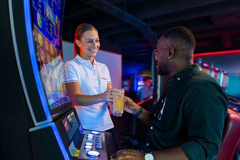 WINWIN Mitarbeiterin serviert einem Gast ein Getränk am Spielautomat