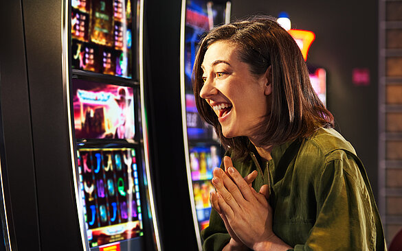 Junge Frau mit schwarzem Haar freut sich im Spielbereich vor einem VLT.