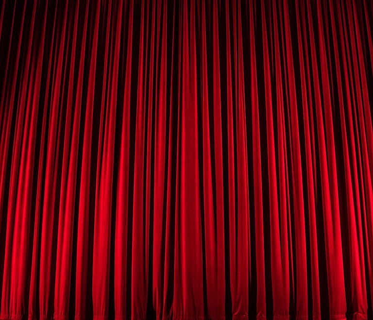 Roter Vorhang auf beleuchteter Buehne.