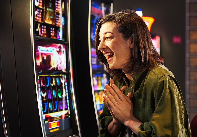 Junge Frau mit schwarzem Haar freut sich im Spielbereich vor einem VLT.