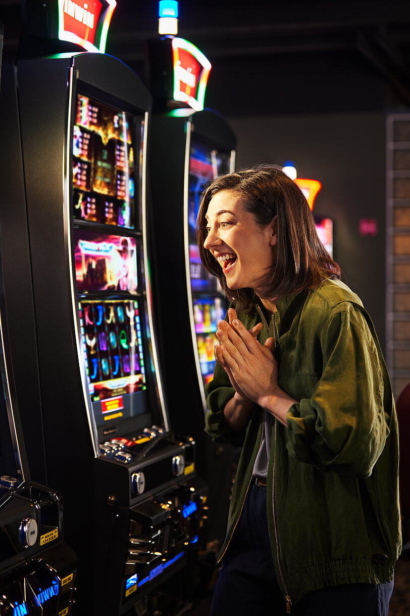 Junge Frau mit schwarzem Haar freut sich im Spielbereich vor einem VLT.