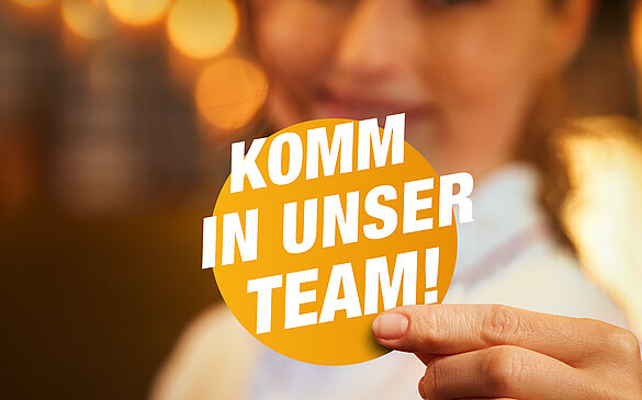 WINWIN-Mitarbeiterin haelt gelben Kreis mit Text: Komm in unser Team!