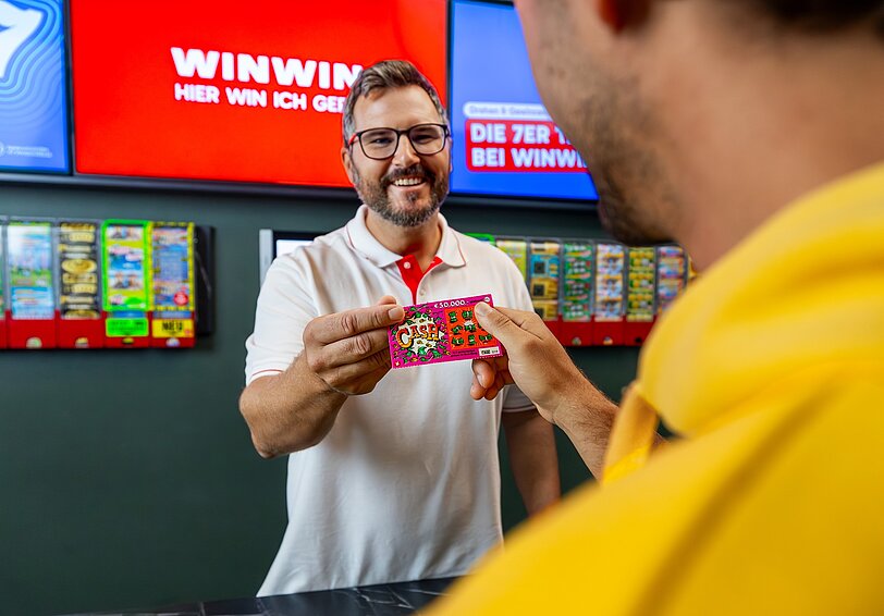 Ein WINWIN Mitarbeiter überreicht einem Gast ein Rubbellos