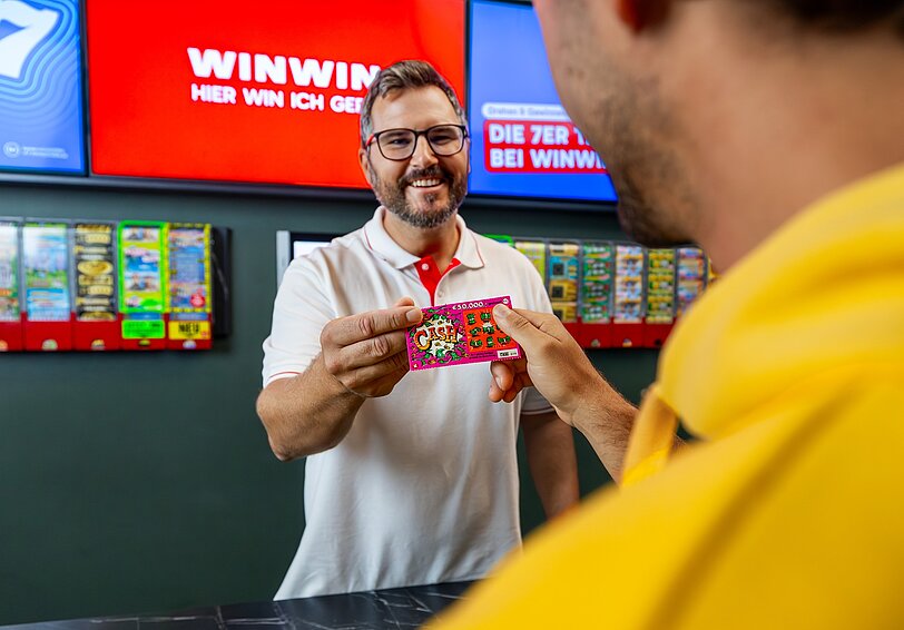 Ein WINWIN Mitarbeiter überreicht einem Gast ein Rubbellos