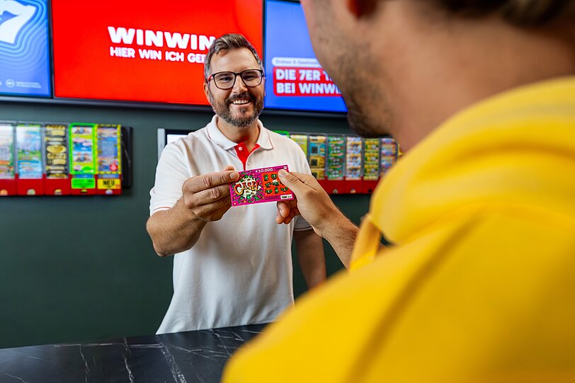 Ein WINWIN Mitarbeiter überreicht einem Gast ein Rubbellos