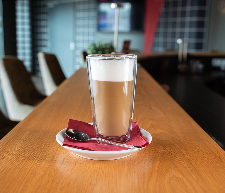 Ein Kaffee mit Milchschaum in einem hohen Glas