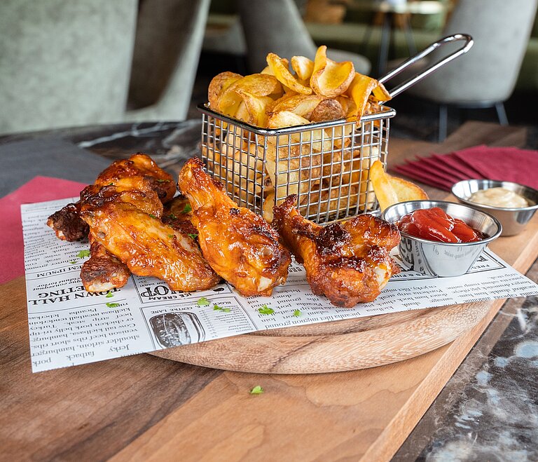 Man sieht Chicken Wings, Pommes und 2 Dips