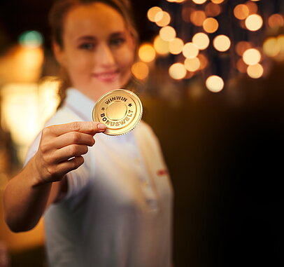 WINWIN-Mitarbeiterin haelt die goldene Bonuswelt-Muenze.