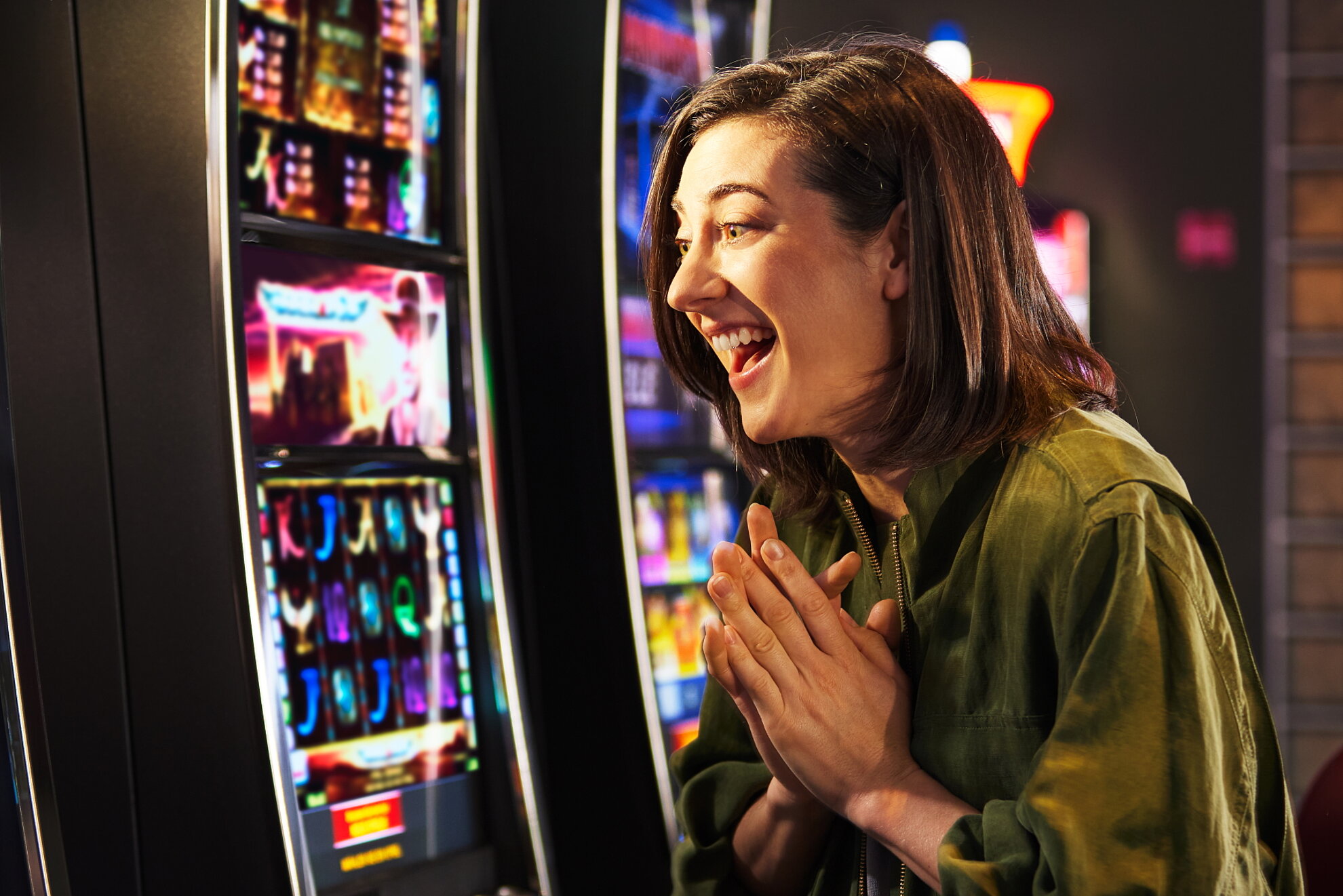 Junge Frau mit schwarzem Haar freut sich vor Spielautomat.