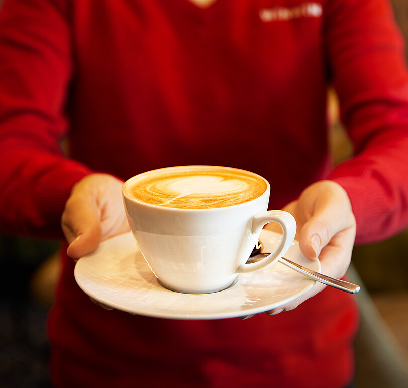WINWIN Mitarbeiterin serviert Kaffee mit Latte-Art Milchschaum.