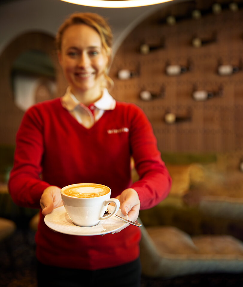 WINWIN Mitarbeiterin serviert Kaffee mit Latte-Art Milchschaum.