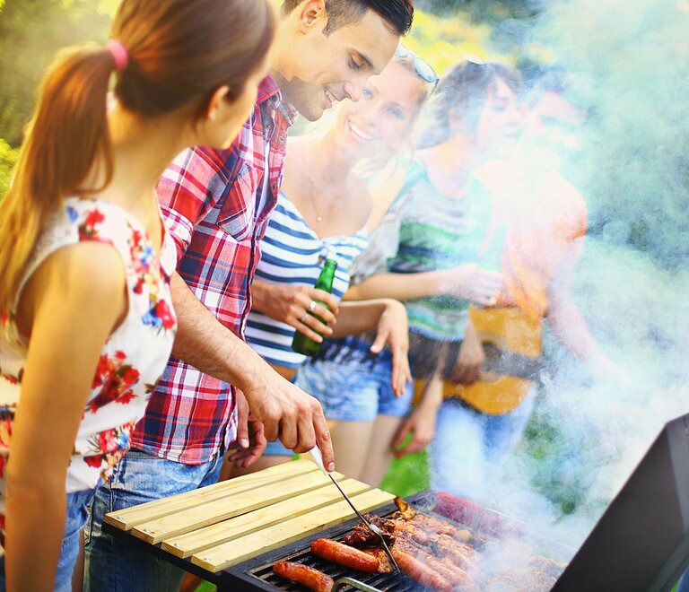 Personen die gemeinsam grillen. Weißer Rauch verdeckt den Hintergrund ein wenig.