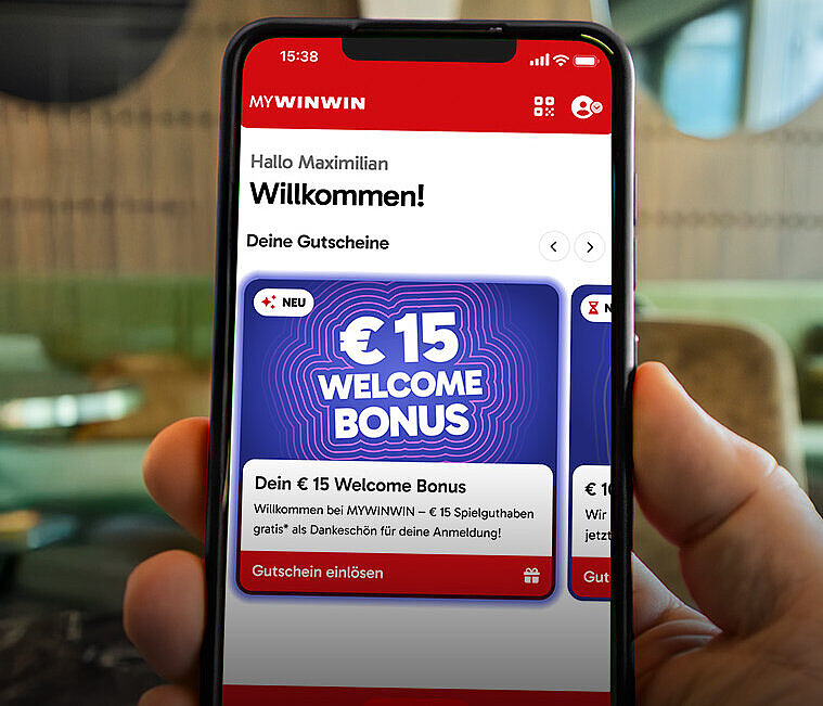 Es wird ein Smartphone gehalten, dessen Screen die Applikation MYWINWIN und den Welcome Bonus zeigt