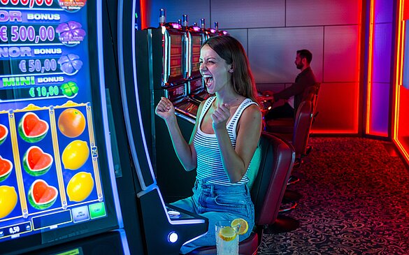 Junge Frau sitzt vor einem Spielautomat und freut sich sehr 