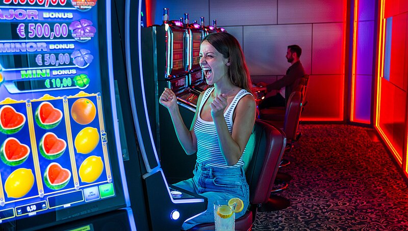Junge Frau sitzt vor einem Spielautomat und freut sich sehr 