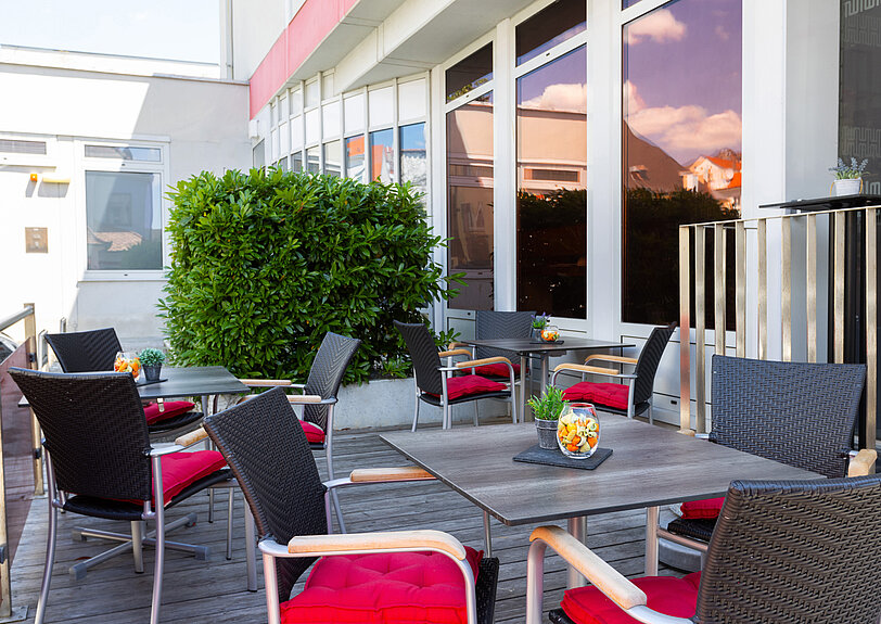 Holzterrasse mit gepolsterten schwarzen Loungestuehlen und Tischdeko vor dem WINWIN Krems.