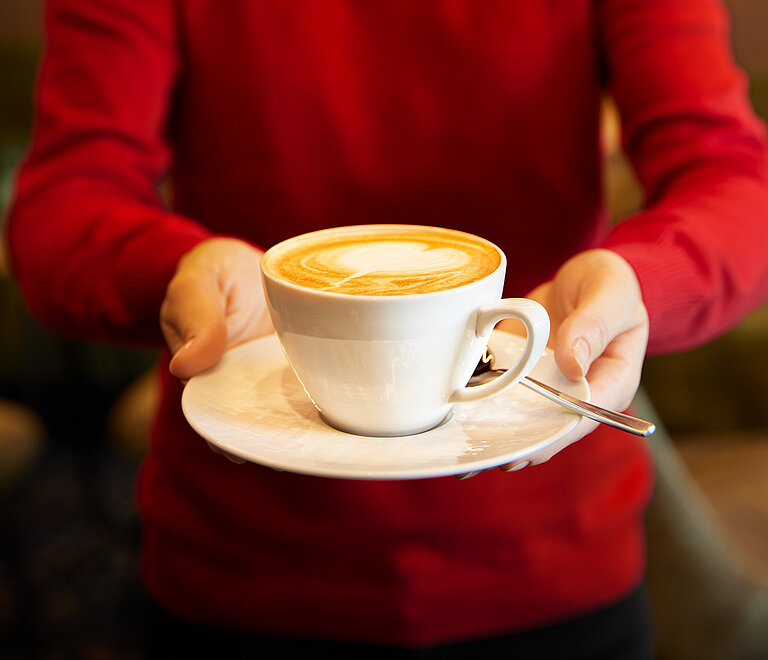 WINWIN Mitarbeiterin serviert Kaffee mit Latte-Art Milchschaum.