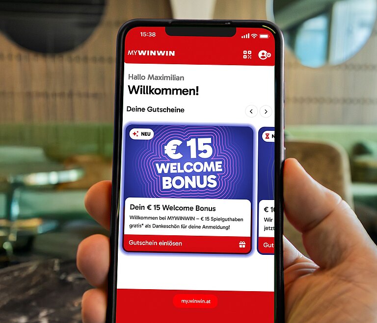 Es ist ein Handy zu sehen, auf dem der Welcome Bonus in der MYWINWIN Applikation gezeigt wird. 