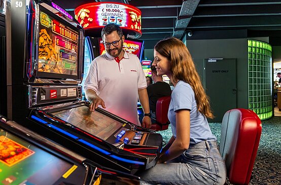 Ein WINWIN Mitarbeiter erklärt einem Gast das Spielen am Video Lottery Terminal