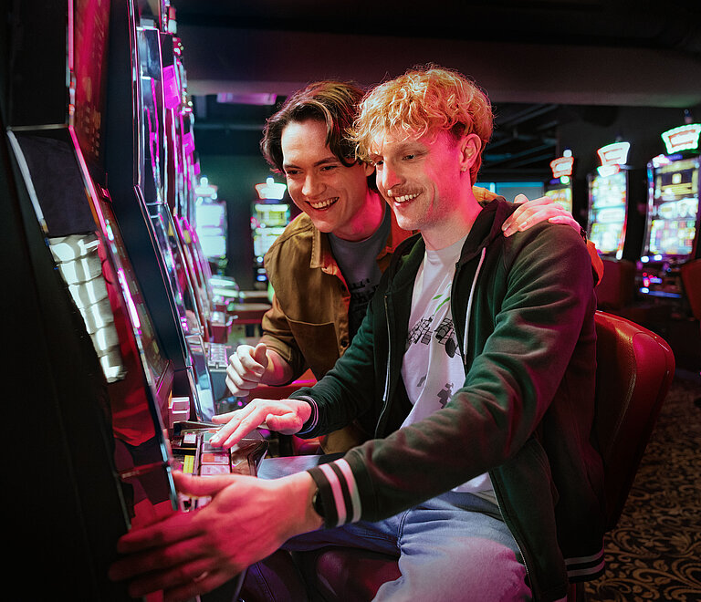 Zwei junge Männer, die an einem Automat spielen.
