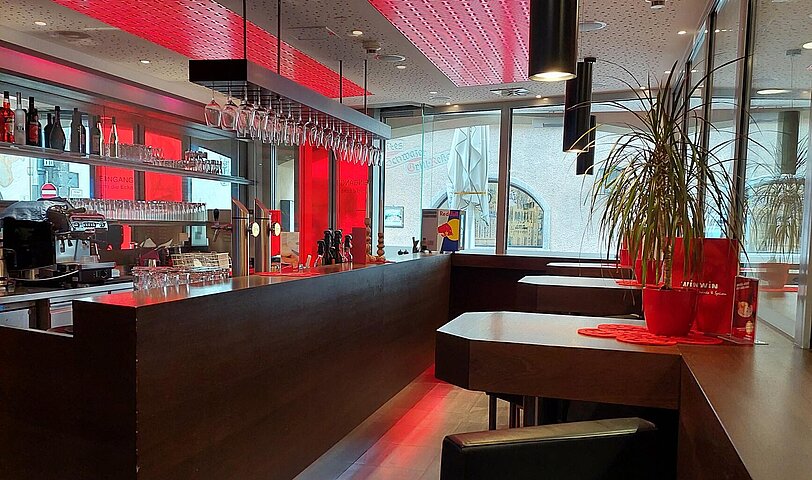 Der rot beleuchtete Barbereich im WINWIN Schwaz mit lederbezogenen Hochstuehlen.