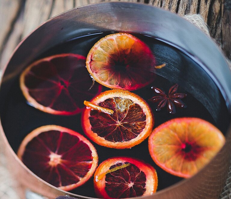 Gluehwein mit Orangen und Gewuerzen in Topf auf dekoriertem Holztisch.
