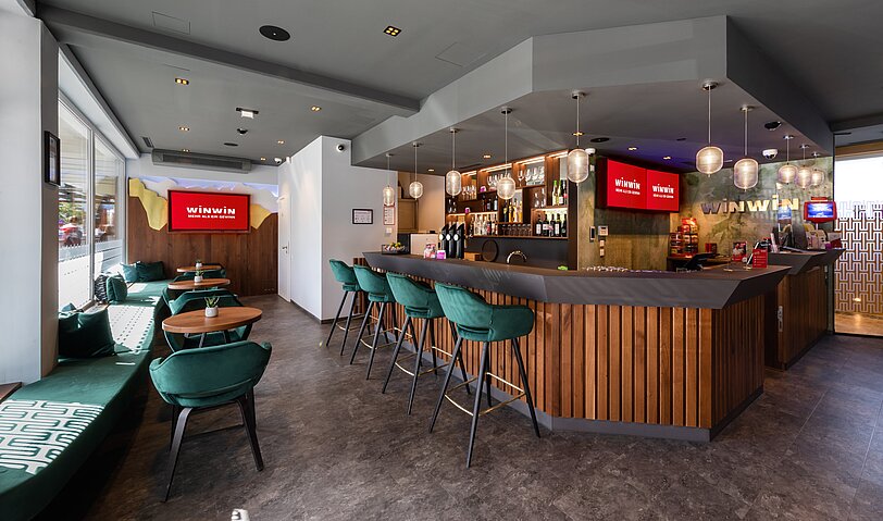 Designer-Bar und smaragdgruene Stuehle im Gastronomiebereich von WINWIN Innsbruck. 