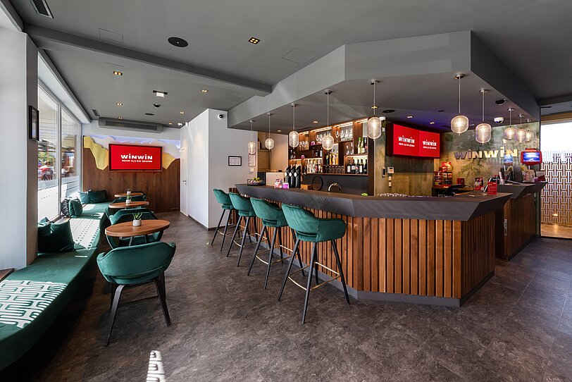 Designer-Bar und smaragdgruene Stuehle im Gastronomiebereich von WINWIN Innsbruck. 