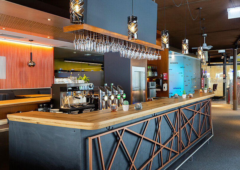 Designer-Bar mit Massivholz-Theke und anthrazitfarbener Front mit Kupfer-Metall-Deko im WINWIN Lienz. 