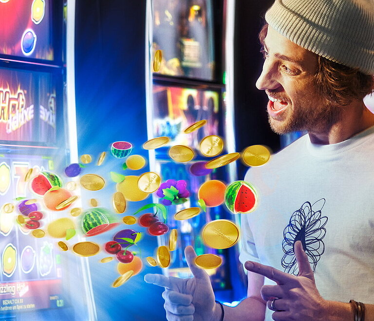 Junger Mann mit Haube zeigt auf Spielautomat mit fliegenden Slot Game-Fruechten.