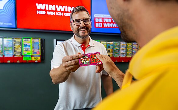 Ein WINWIN Mitarbeiter überreicht einem Gast ein Rubellos