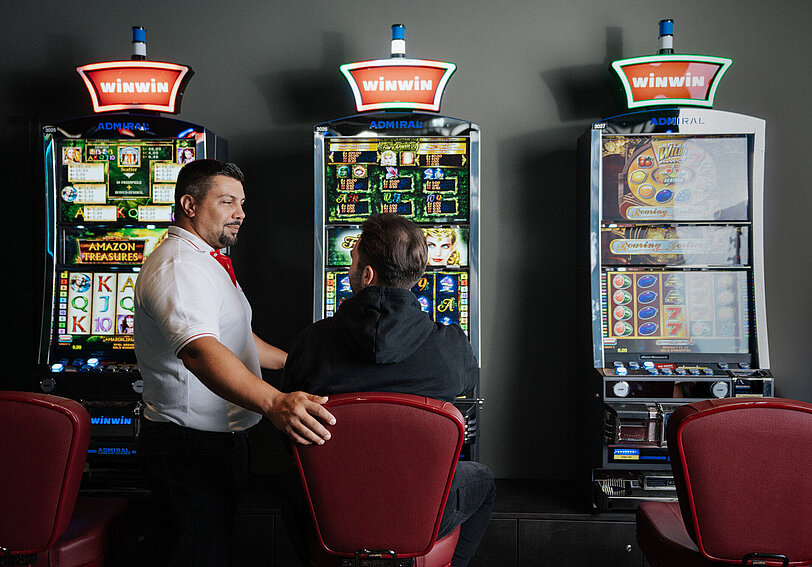 Ein WINWIN Mitarbeiter betreut einen Gast am Spielautomat